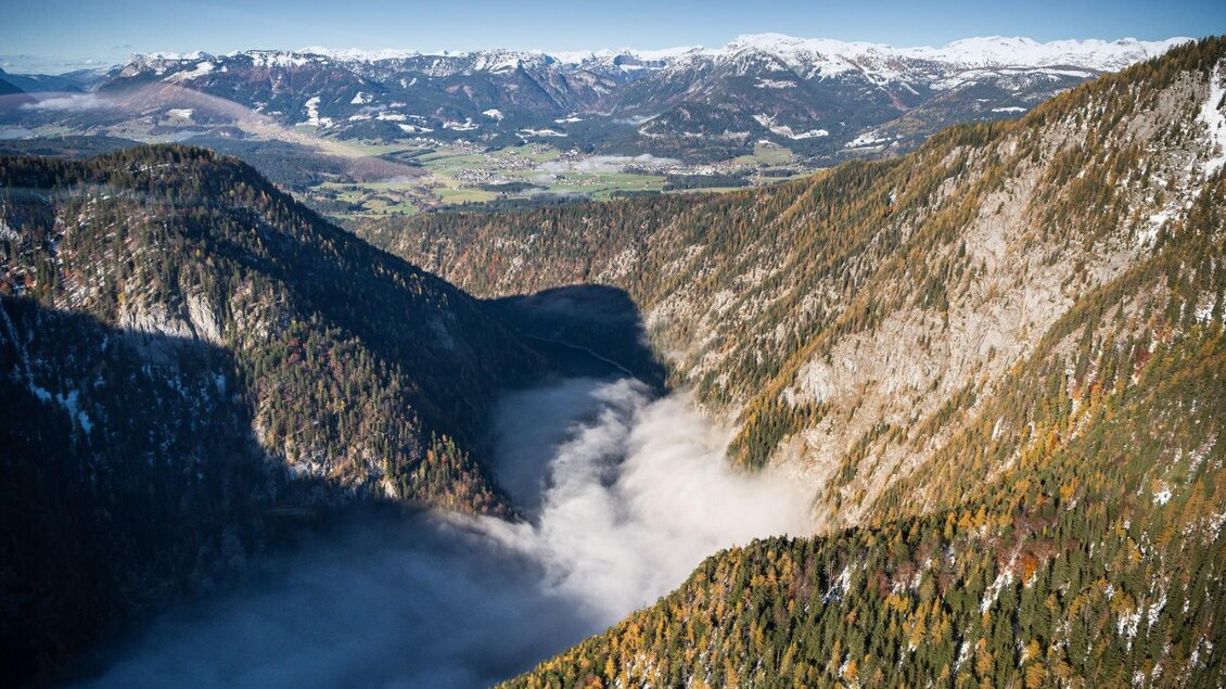 Eine spektakuläre Berglandschaft mit tiefen Tälern und schneebedeckten Gipfeln. Nebel schwebt sanft über dem Tal und schafft eine mystische Atmosphäre.