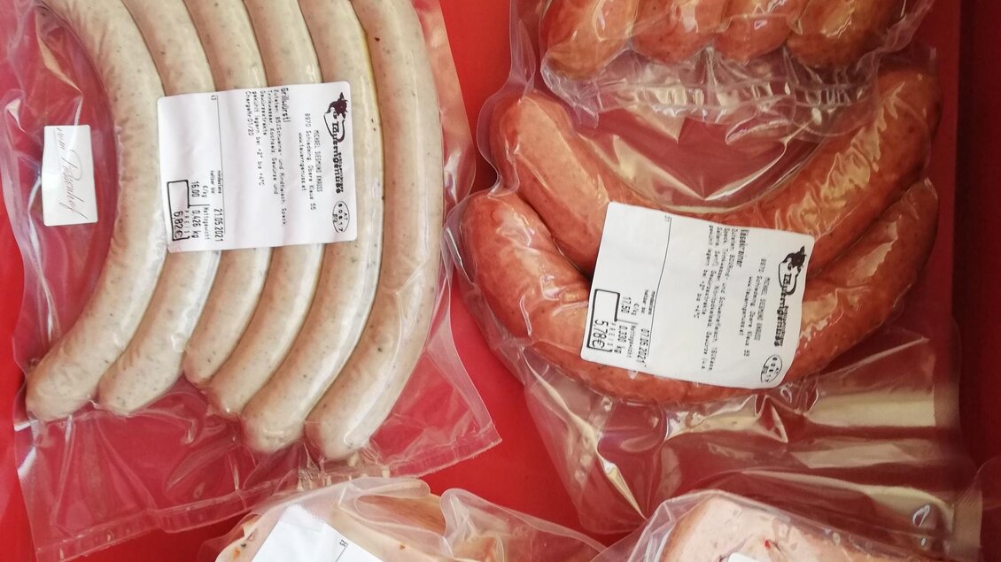 Eine Auswahl an verpackten Würstchen und Fleischprodukten in durchsichtigen Beuteln. Die Produkte liegen auf einem roten Hintergrund. | © Markus Putz