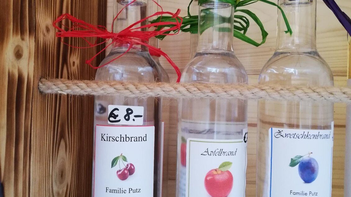 Mehrere Flaschen mit Obstbränden stehen auf einem Holzregal. Jede Flasche hat ein Etikett mit dem Namen des Obstes und dem Preis. | © Markus Putz