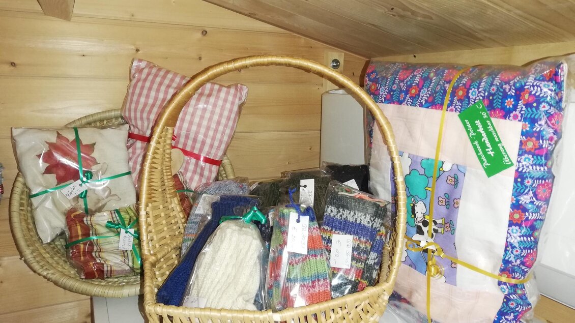 Ein Korb voller handgemachter Geschenke und Kissen in einem rustikalen Holzraum. Die Verpackungen sind farbenfroh und festlich dekoriert. | © Markus Putz