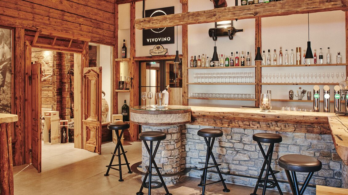 Eine gemütliche Bar mit Holzdekor und einer Steinmauer. Die Theke ist mit mehreren Sitzplätzen ausgestattet und hinter der Bar stehen verschiedene Getränke. | © Felix Werinos