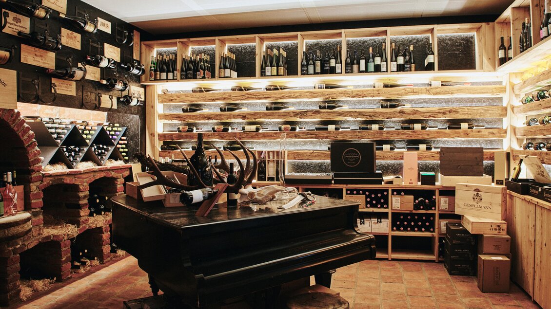 Ein stilvoller Weinkeller mit Regalen voller Weinflaschen. In der Mitte steht ein runder Tisch mit Stühlen und einem klassischen Weinzubehör. | © Felix Werinos