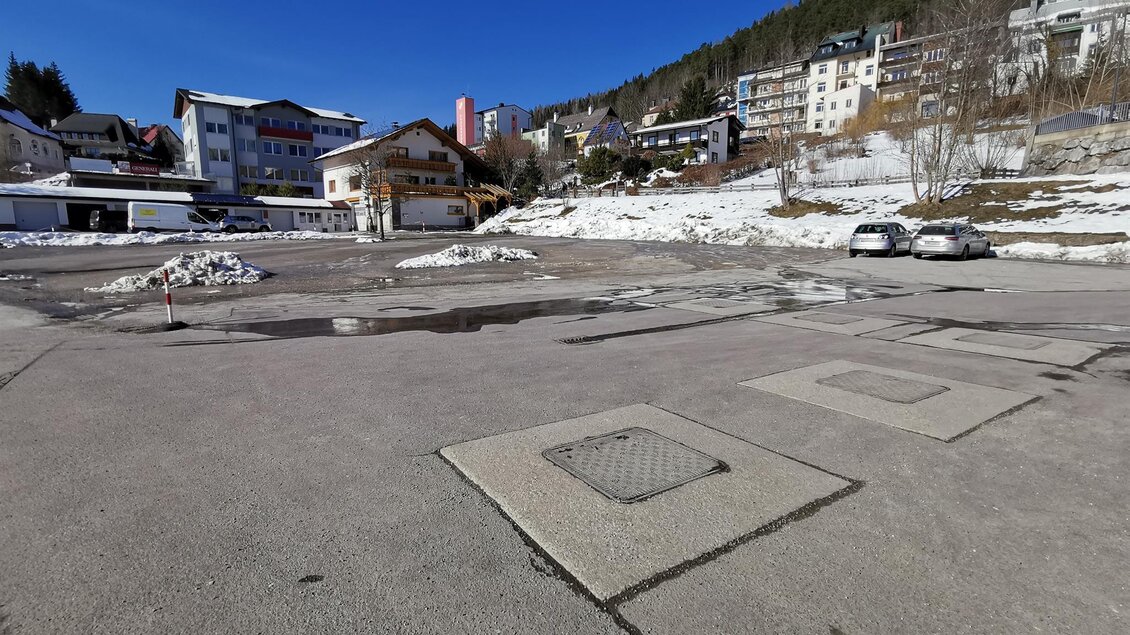 Eine leere Fläche mit schneebedecktem Boden und einigen sichtbaren Häusern im Hintergrund. Der Himmel ist klar und blau. | © TV Hochsteiermark / Brigitte Digruber