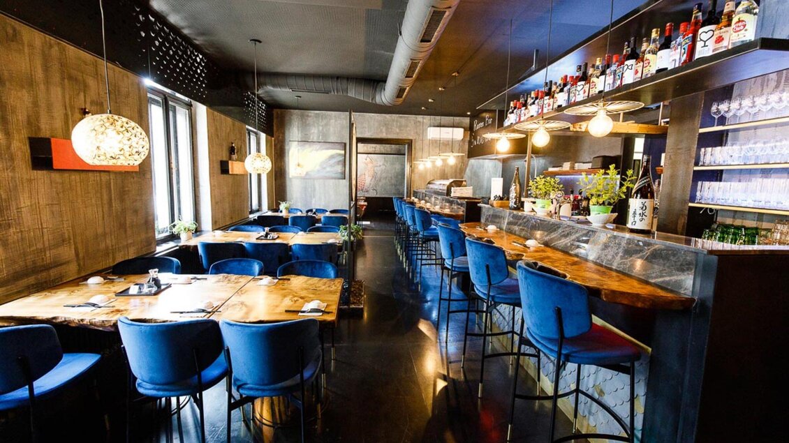 Ein modernes Restaurant mit stilvollen blauen Stühlen und Holztischen. Die Bar im Hintergrund ist gut ausgestattet und lädt zum Verweilen ein. | © Sakana