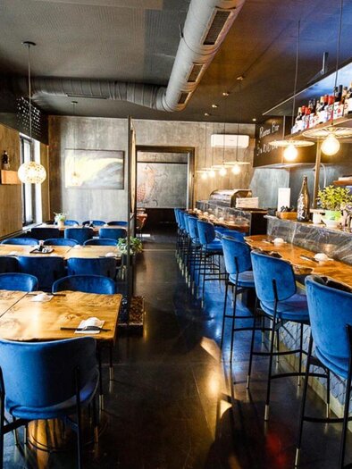 Ein modernes Restaurant mit stilvollen blauen Stühlen und Holztischen. Die Bar im Hintergrund ist gut ausgestattet und lädt zum Verweilen ein. | © Sakana