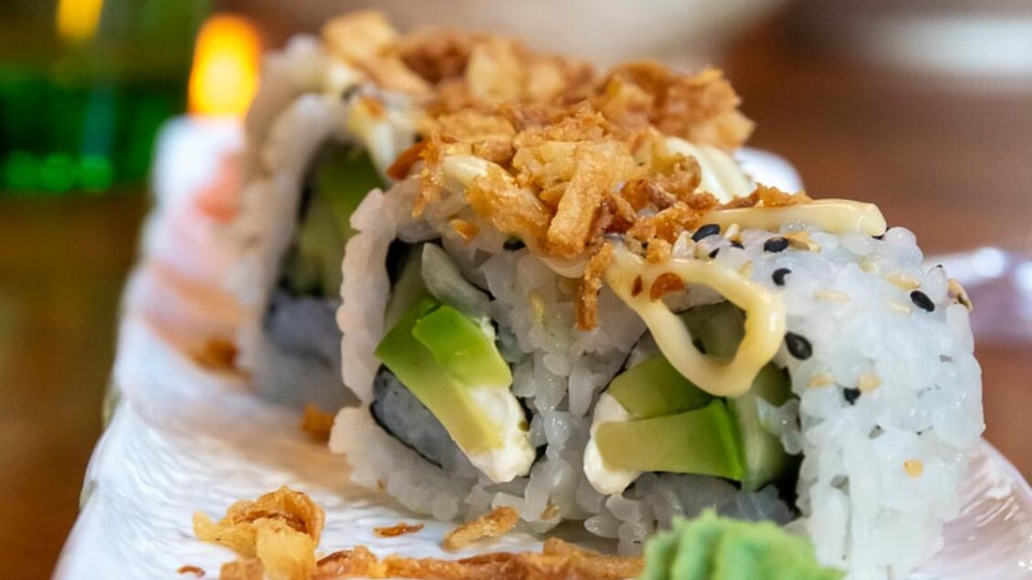 Leckeres Sushi mit Reis, Avocado und knusprigen Zwiebelringen. die Rollen sind mit einer cremigen Sauce garniert. | © Sakana