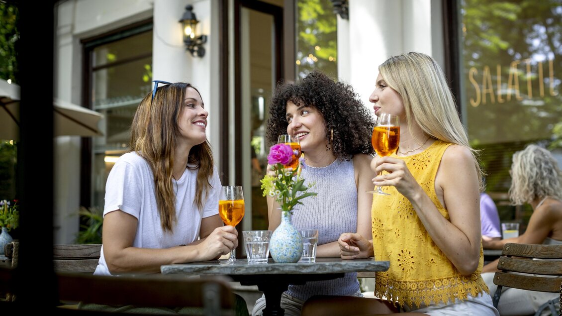  Drei Frauen sitzen draußen am Tisch, unterhalten sich und trinken Aperitif, in der Mitte steht eine Vase mit Blumen. | © Graz Tourismus - Tom Lamm