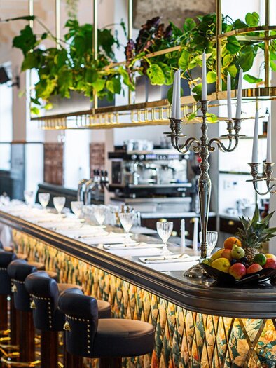 Ein eleganter Restaurantbereich mit einer stilvollen Bar und Pflanzen dekoriert. Tische sind für Gäste vorbereitet, und im Hintergrund sind Getränke sichtbar. | © Weitzer Hotels