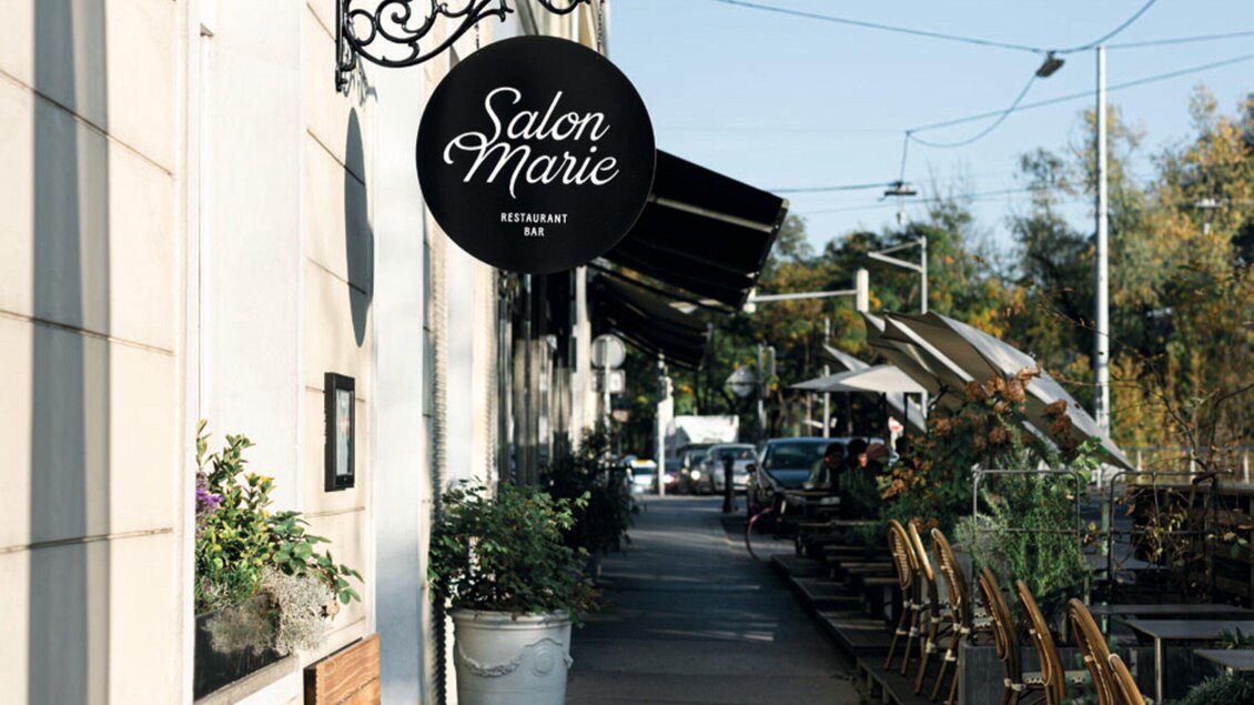 Ein Restaurant mit dem Namen "Salon Marie" befindet sich an einer einladenden Straße. Draußen stehen Tische und Stühle in der Sonne. | © Salon Marie