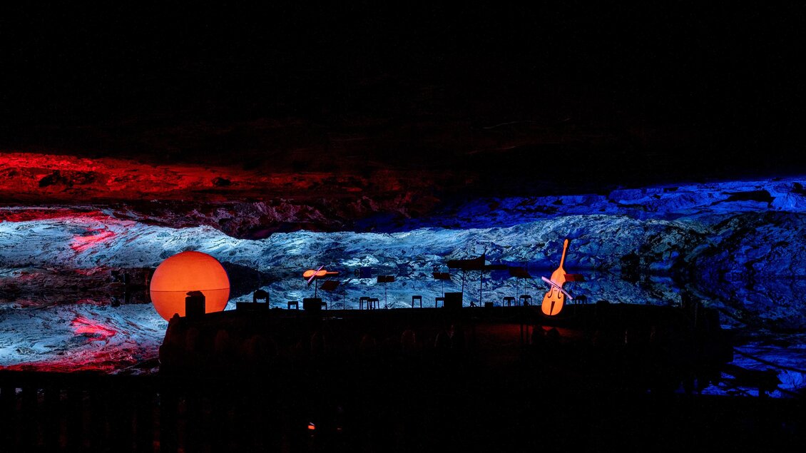 Eine beeindruckende Szene mit bunten Lichtern in einem dunklen Raum. Im Vordergrund sind einige Objekte und eine große orangefarbene Kugel zu sehen. | © Salzwelten - Fotozauber Laimer