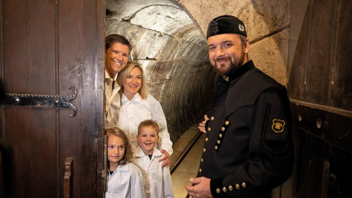 Eine Familie steht vor einem Gewölbe mit einem Führer in historischer Kleidung. Alle lächeln und die Umgebung ist steinern und rustikal. | © Bergauer