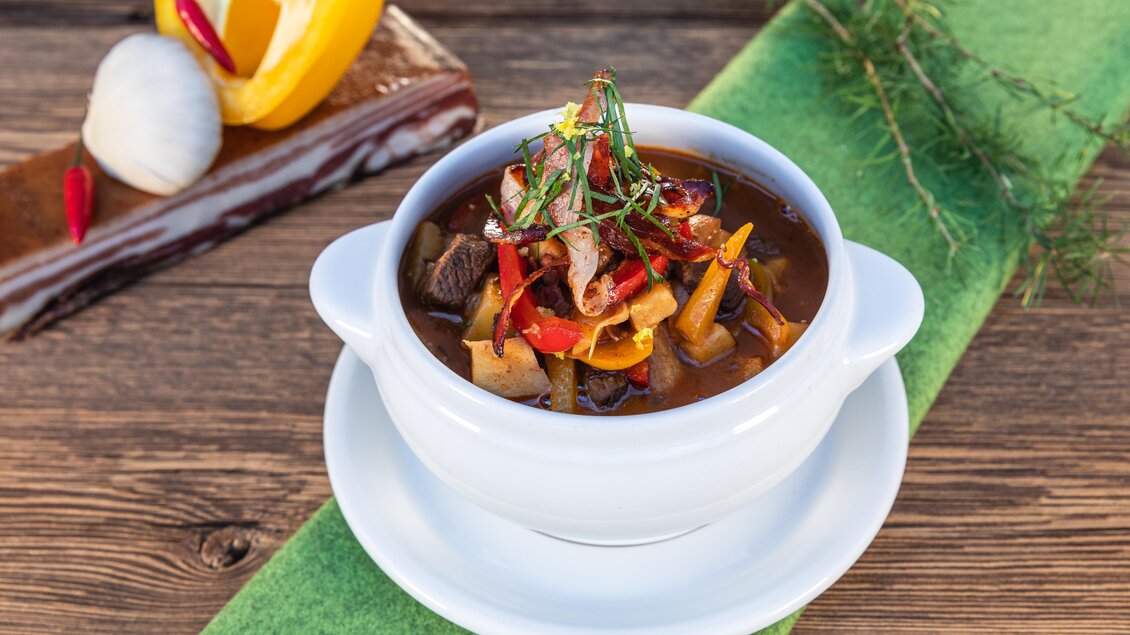 Eine Schüssel mit bunter Gemüsesuppe, garniert mit frischen Kräutern und Chilischoten. Im Hintergrund sind ein Stück gelber Paprika und ein Dessert zu sehen. | © Martin Huber