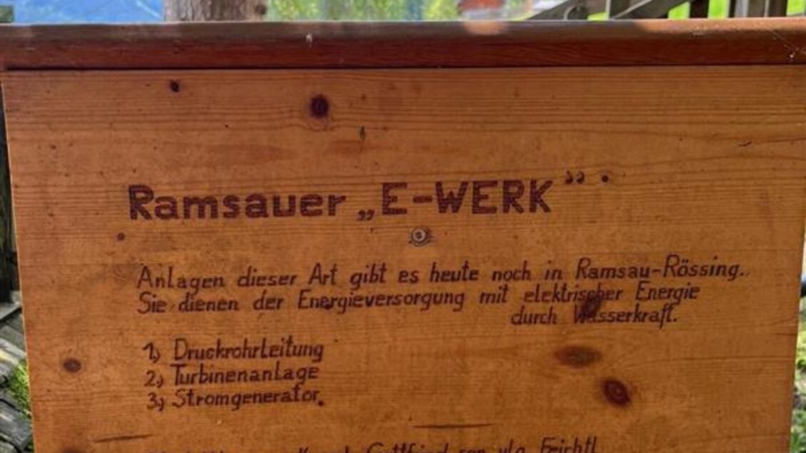 Ein Holzschild mit der Aufschrift "Ramsauer E-Werk". Es beschreibt die Energieversorgung durch Wasserkraft und nennt Details zur technischen Ausführung. | © Sattelberghütte