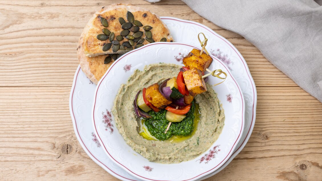 Ein Teller mit einer cremigen Sauce und bunten Gemüse-Spießen. Neben dem Gericht liegen Brotstücke mit Kürbiskernen. | © ©Martin Huber