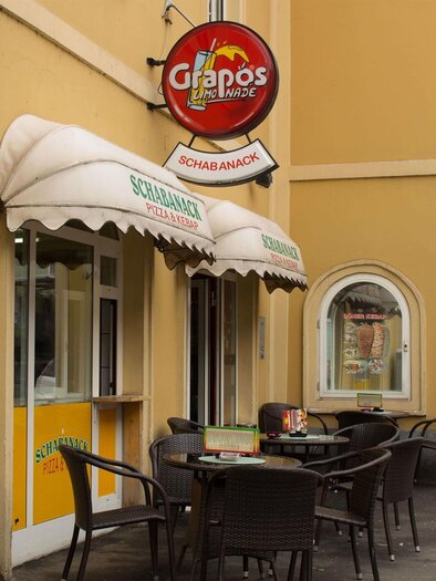A small restaurant with an outdoor area and tables on the street. The walls are painted in bright colors and various signs are visible. | © C. Stein