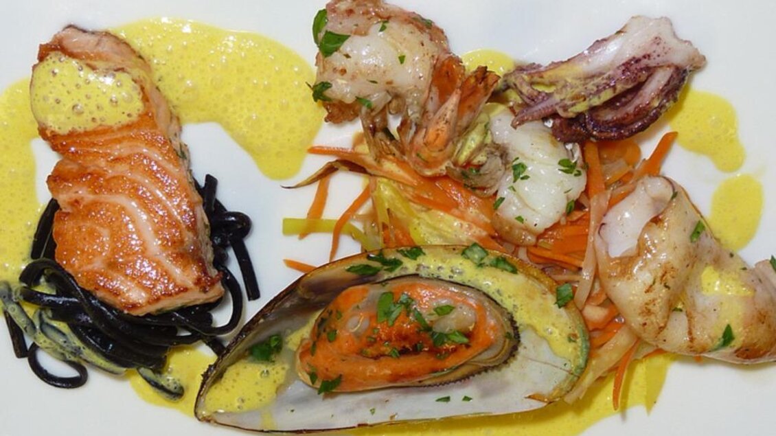 Ein kunstvoll angerichteter Teller mit verschiedenen Meeresfrüchten, darunter Lachs, Garnelen und Muscheln. Dazu gibt es schwarze Nudeln und eine cremige Sauce. | © Schaller's Gastwirtschaft