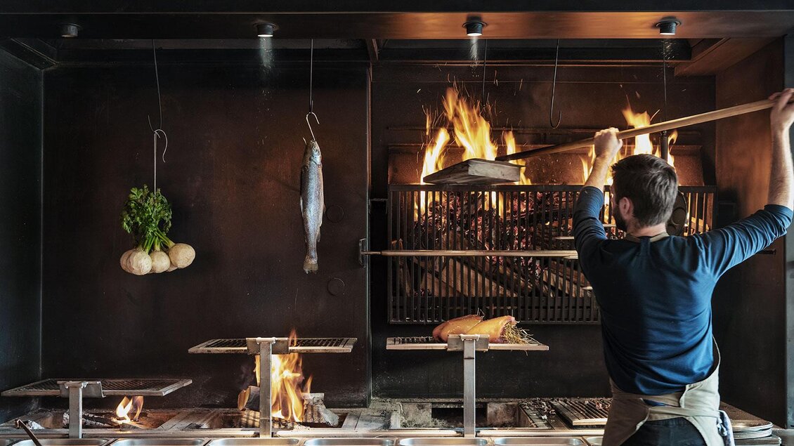 Ein Koch grillt frischen Fisch über einem offenen Feuer. Im Hintergrund sind Gemüse und weitere Zutaten sichtbar. | © Restaurant Steirereck/Cathrine Stukhard