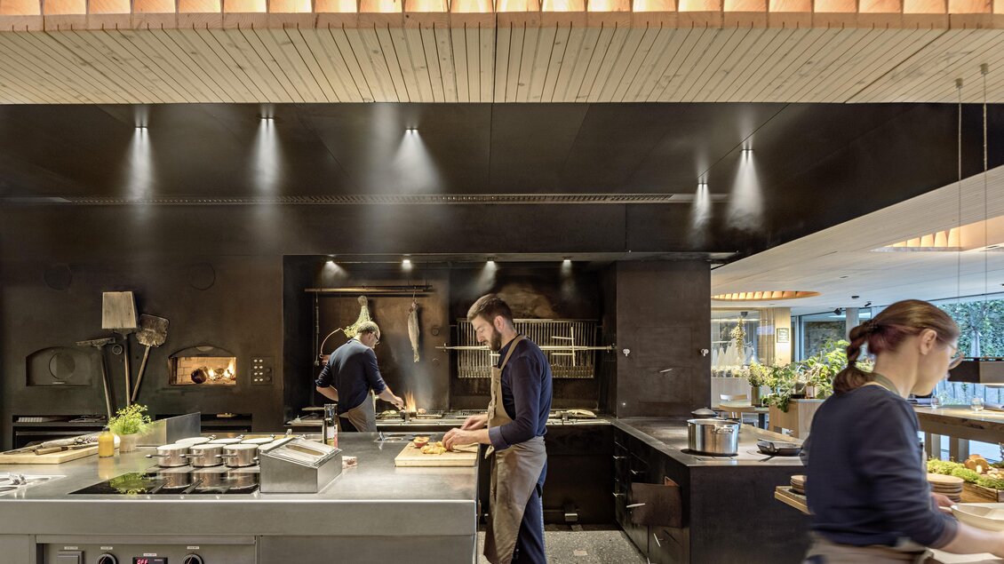 Eine moderne Küche mit zwei Köchen, die mit frischen Zutaten arbeiten. Der Raum ist stilvoll mit Holzakzenten und heller Beleuchtung eingerichtet. | © Restaurant Steirereck/Hertha Hurnaus