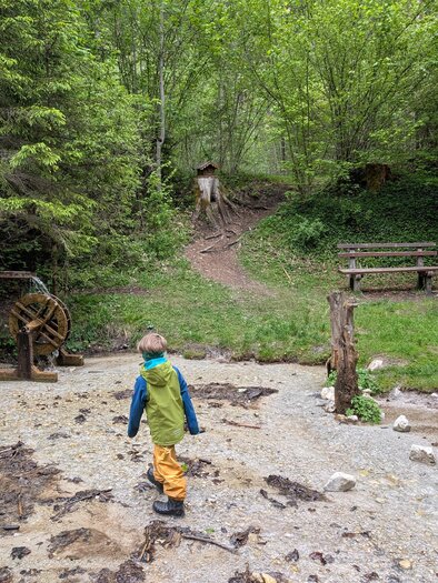 Two children are playing in a wooded area with a watermill. The surroundings are green and inviting with benches for sitting. | © Stefan Wieser-Bliem