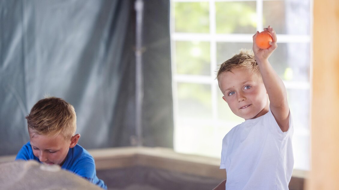 Zwei Kinder spielen in einem Sandkasten. Ein Junge hält einen orangefarbenen Ball hoch. | © www. Zloam.at