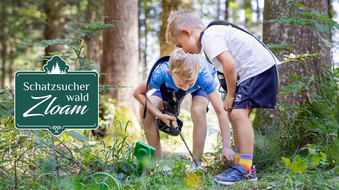 Zwei Kinder erkunden den Wald und suchen nach Schätzen. Sie sehen aufmerksam auf den Boden, um etwas Interessantes zu finden. | © www.zloam.at