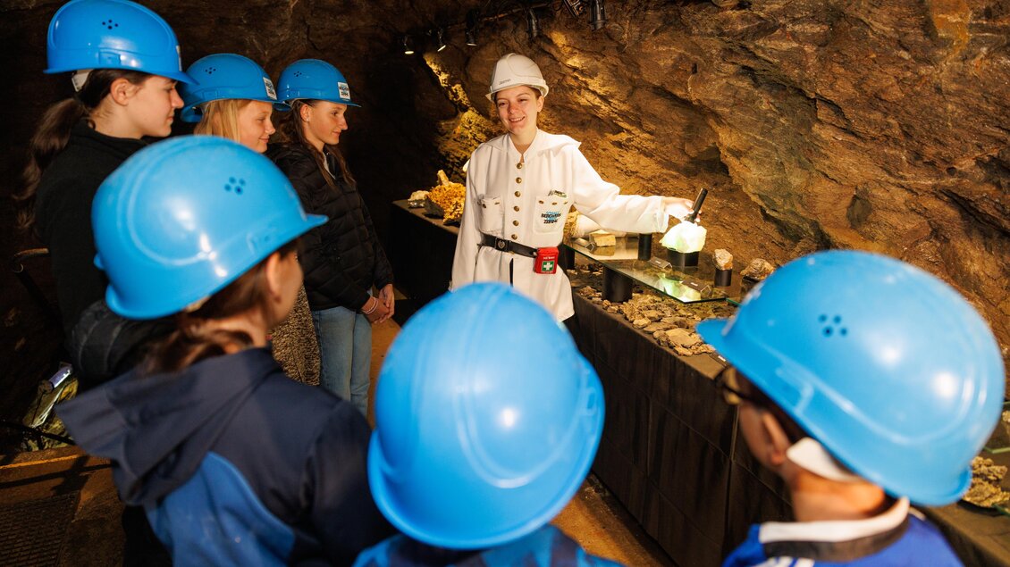 Eine Gruppe von Kindern in blauen Helmen hört einem Führer in einer Höhle zu. Der Führer erklärt wahrscheinlich etwas über Mineralien oder die Umgebung. | © Anita Fössl