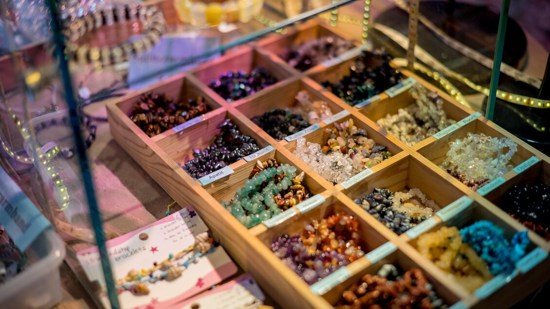 Ein Schmuckdisplay mit verschiedenen Armbändern aus bunten Steinen. Die Armbänder sind in Holzkästen organisiert. | © Anita Fössl