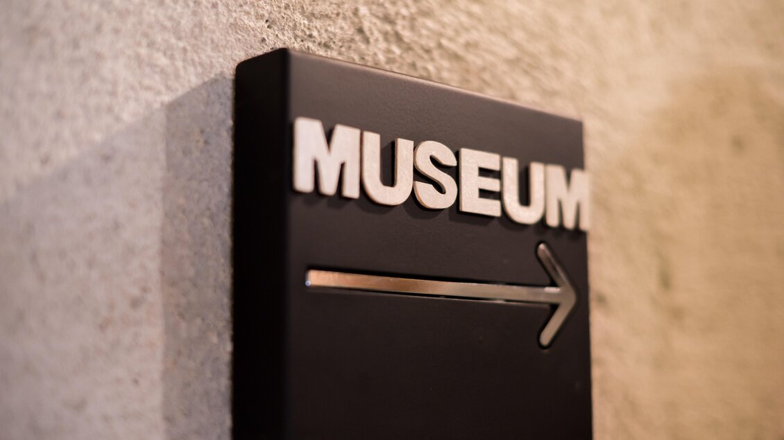 Ein schwarzes Schild mit dem Wort "MUSEUM" und einem Pfeil nach rechts. Es zeigt den Weg zum Museum an. | © Anita Fössl