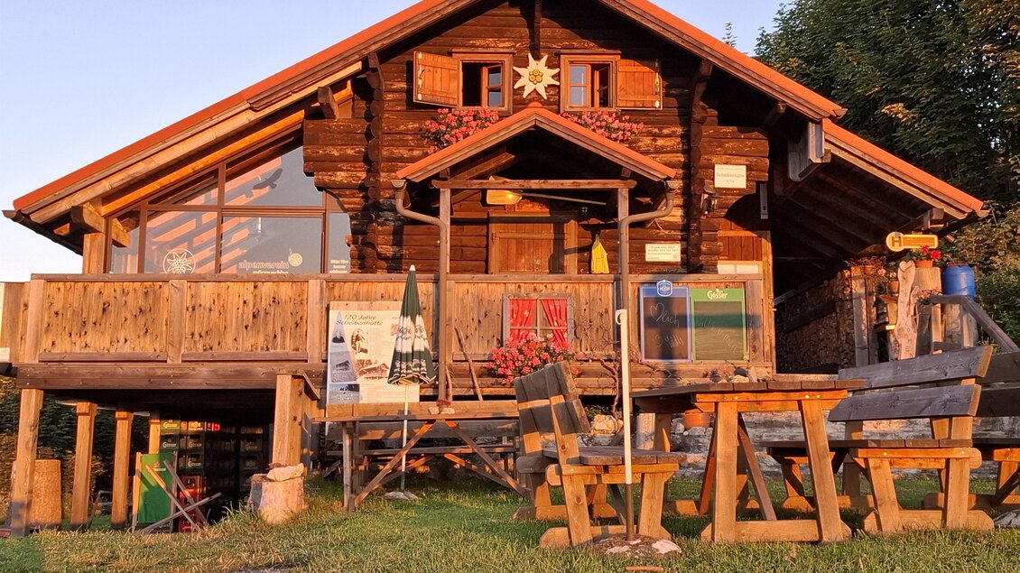 Ein gemütliches Holzhaus mit Terrasse und schönen Verzierungen. Vor dem Haus stehen mehrere Holzmöbel in einer grünen Wiese.