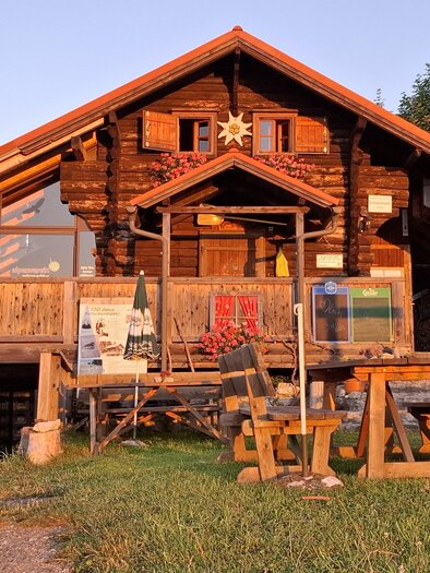 Ein gemütliches Holzhaus mit Terrasse und schönen Verzierungen. Vor dem Haus stehen mehrere Holzmöbel in einer grünen Wiese.