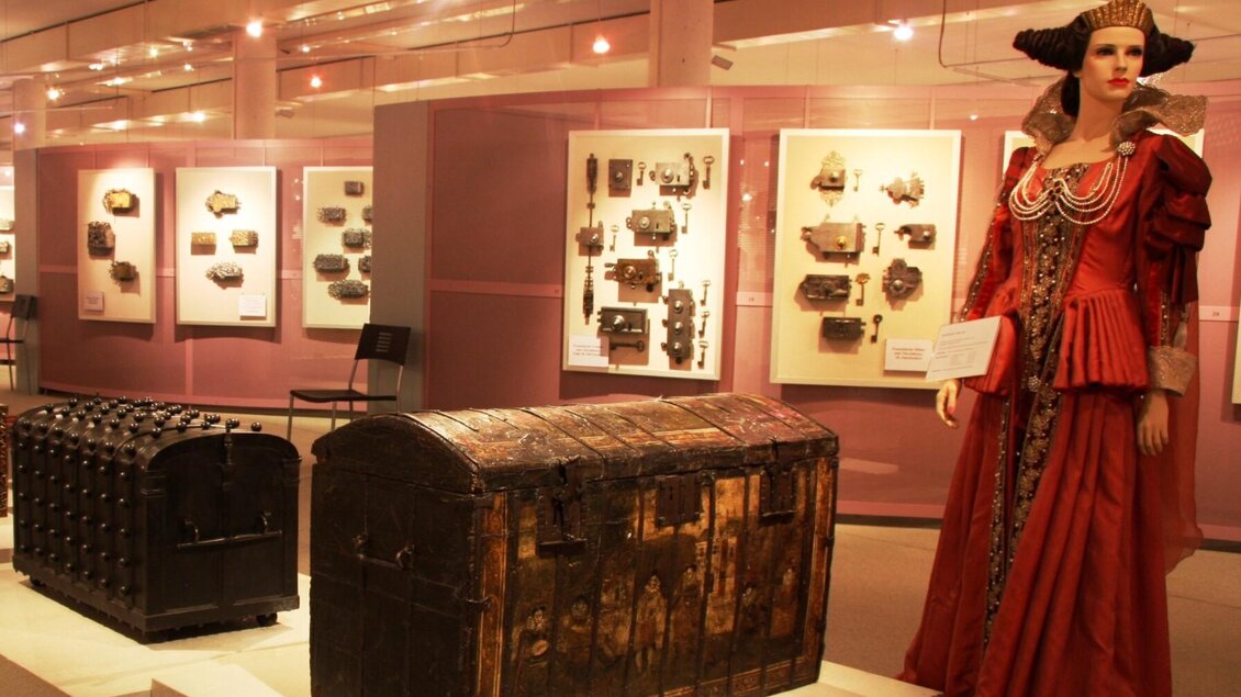 Ausstellung mit alten Truhen, Schlössern und einer Puppe in historischer Damenkleidung in der Schell Collection Graz. | © Schell Collection