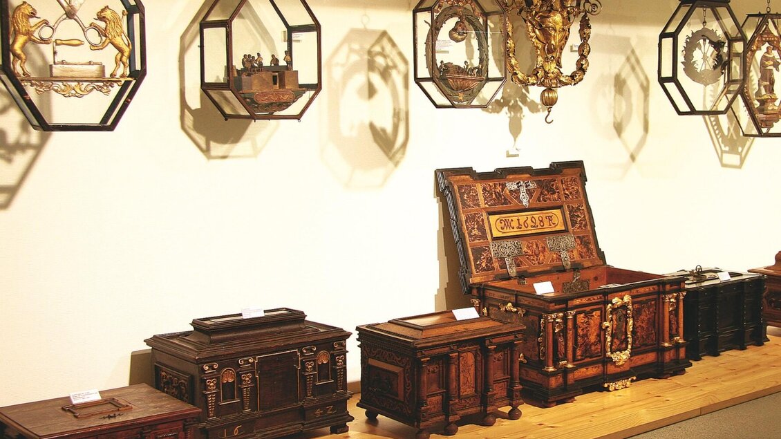 Aufgereihte historische Truhen und hängende Zunftzeichen in der Schell Collection in Graz.  | © Schell Collection