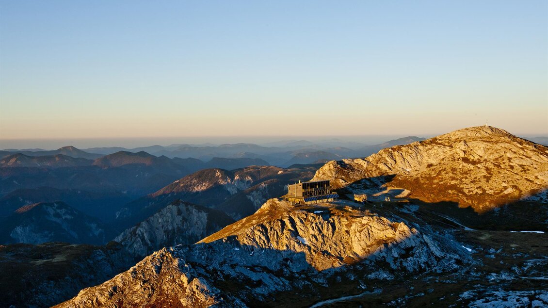 Eine beeindruckende Berglandschaft bei Sonnenuntergang. Im Vordergrund sind schneebedeckte Felsen und im Hintergrund erstrecken sich weitere Berge.