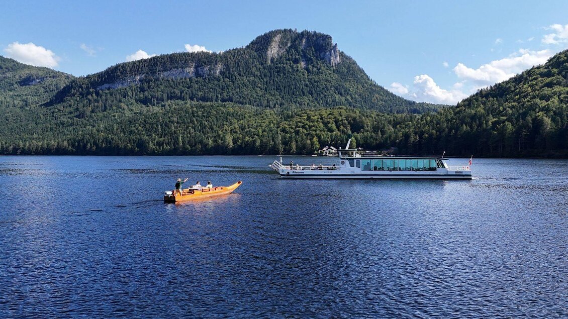 Ein ruhiger See umgeben von grünen Bergen. Ein Kanu und ein Ausflugsschiff sind auf dem Wasser zu sehen. | © Altaussee Schifffahrt