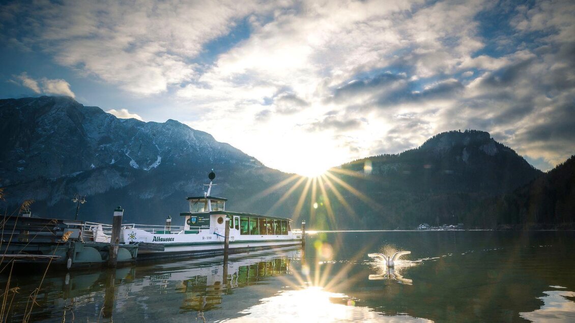 Ein schöner See mit einem Boot im Vordergrund. Die Sonne scheint durch die Wolken und reflektiert auf dem Wasser. | © Rudi Kain