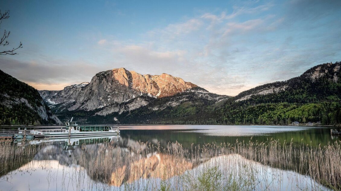 Ein schöner See mit spiegelndem Wasser und umliegenden Bergen. In der Nähe liegt ein Bootsanleger mit einem Schiff. | © Rudi Kain