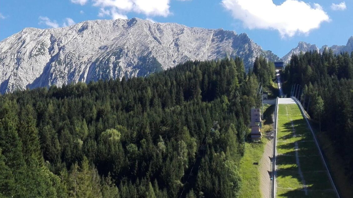 Ein malerisches Bergpanorama mit schneebedeckten Gipfeln und dichten Wäldern. Im Vordergrund ist eine Skipiste zu sehen, die sich durch die Landschaft zieht. | © TVB Ausseerland Salzkammergut/Raunigg
