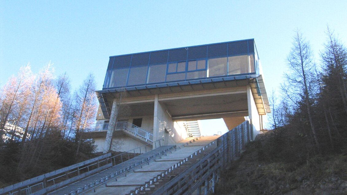 Ein modernes Gebäude auf einem Hang, umgeben von Nadelbäumen. Die Architektur ist schlicht und funktional, mit einer breiten Treppe, die zum Eingang führt. | © TVB Ausseerland Salzkammergut/Rastl