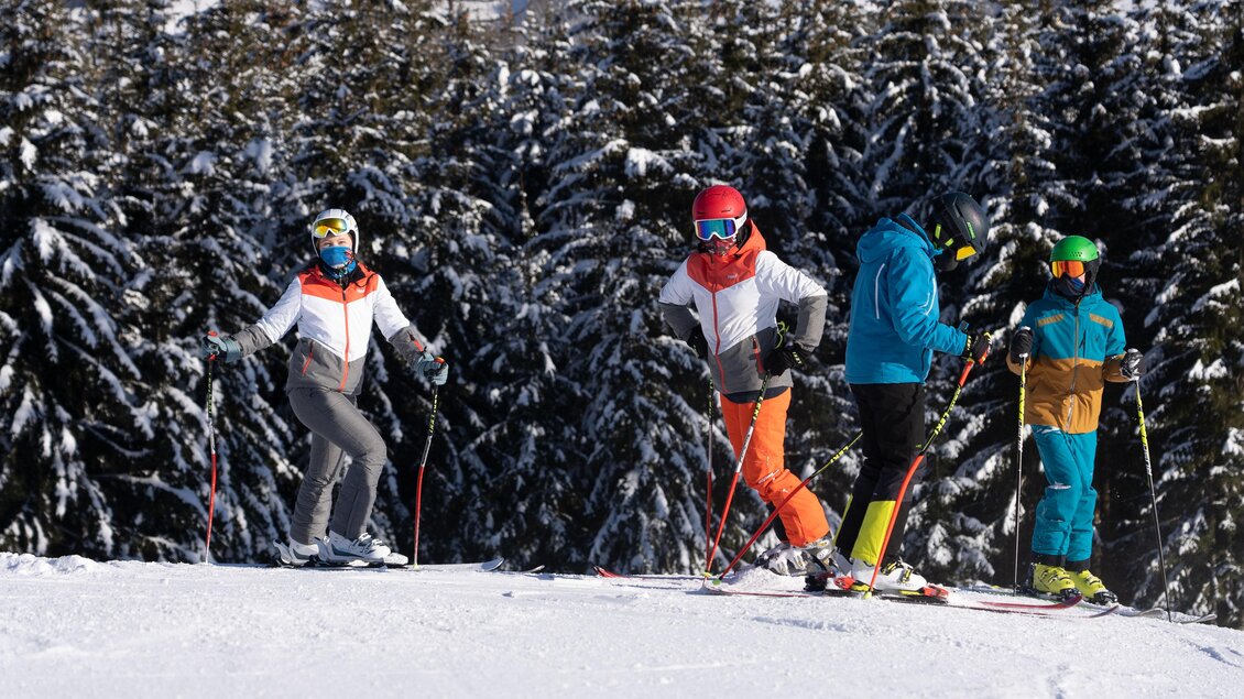Eine Gruppe von Skifahrern steht auf einer schneebedeckten Piste. Im Hintergrund sind grüne Tannenbäume zu sehen. | © Schilift Obdach