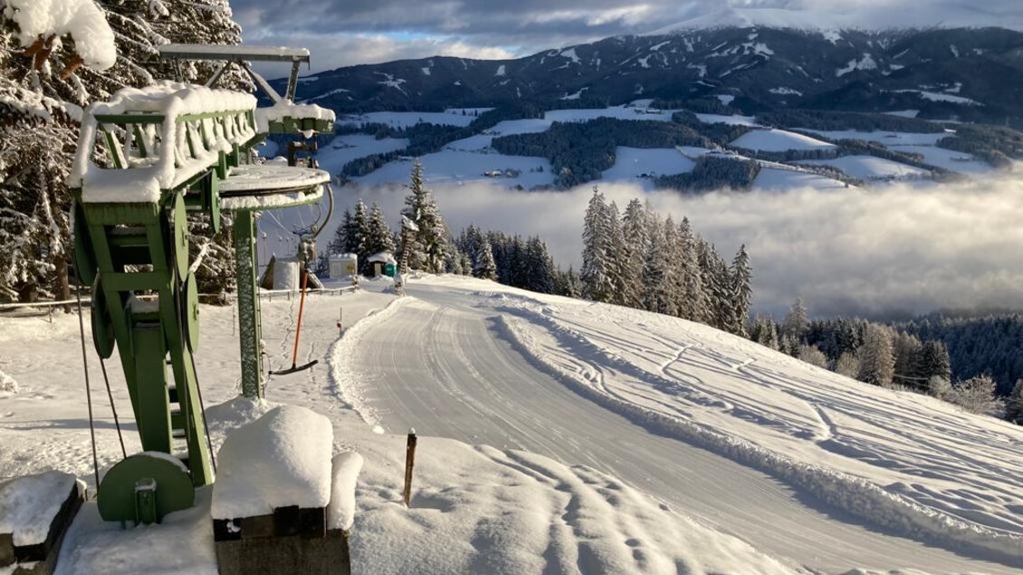 Eine verschneite Berglandschaft mit einem Skilift im Vordergrund. Im Hintergrund sind bewaldete Berge und Wolken sichtbar. | © Schilift Obdach