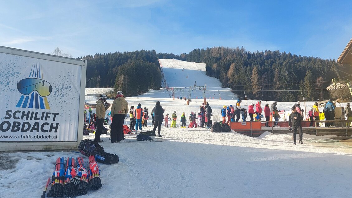 Ein Skigebiet mit vielen Menschen, die auf den Skipisten stehen. Im Hintergrund sind die verschneiten Hänge und ein blauer Himmel zu sehen. | © Schilift Obdach