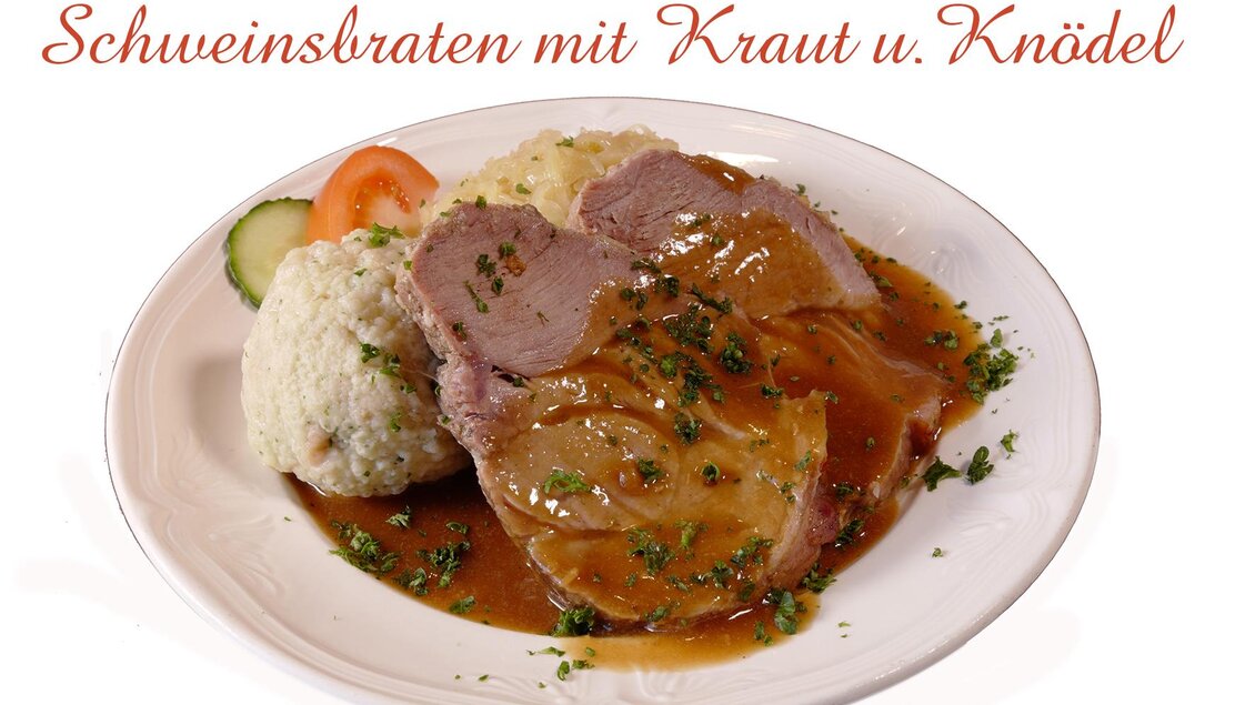 Ein Teller mit Schweinsbraten, serviert mit Kraut und Knödel. Das Gericht ist mit Soße und frischen Kräutern garniert. | © Foto TOM