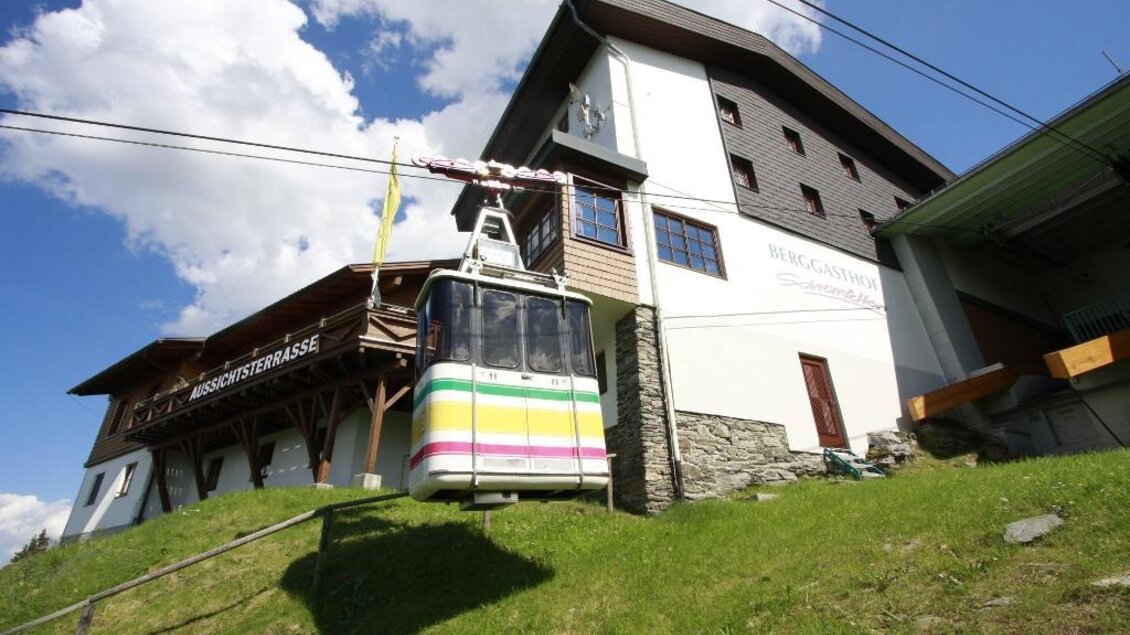 Eine Bergbahn fährt zu einem Gebäude im Grünen. Im Hintergrund sind blauer Himmel und einige Wolken zu sehen. | © Verein Schaferlebnis am Hauser Kaibling