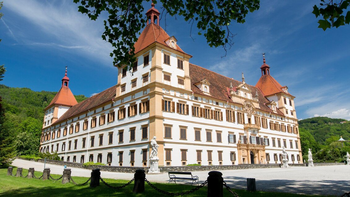 Ein beeindruckendes Schloss mit roten Dächern und einer schönen Fassade. Umgeben von grüner Landschaft und blauen Himmel. | © Graz Tourismus - Harry Schiffer