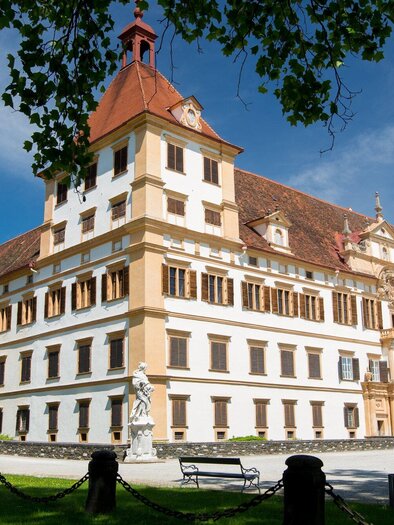 Ein beeindruckendes Schloss mit roten Dächern und einer schönen Fassade. Umgeben von grüner Landschaft und blauen Himmel. | © Graz Tourismus - Harry Schiffer