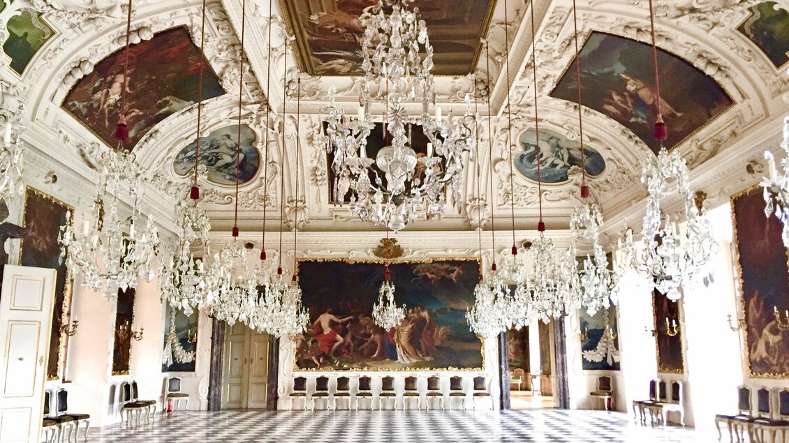 Ein prächtiger Saal mit kunstvollen Deckenmalereien und eleganten Kronleuchtern. Der Boden ist mit schwarz-weißen Fliesen ausgelegt und die Wände sind mit historischen Gemälden geschmückt. | © Keith Jenkins - Velvet Escape