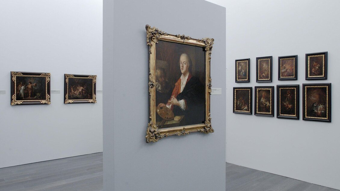 Ein Ausstellungsraum mit mehreren Bildern an den Wänden. Im Vordergrund hängt ein großes Gemälde in einem goldenen Rahmen. | © UMJ