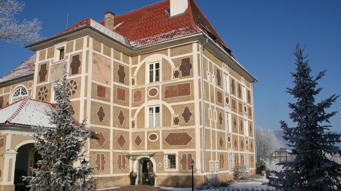 Ein historisches Gebäude mit hübscher Fassade und rotem Dach. Im Vordergrund sind schneebedeckte Bäume zu sehen. | © Schloss Farrach