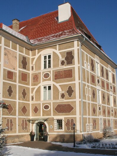 A historical building with a beautiful facade and a red roof. In the foreground, snow-covered trees can be seen. | © Schloss Farrach