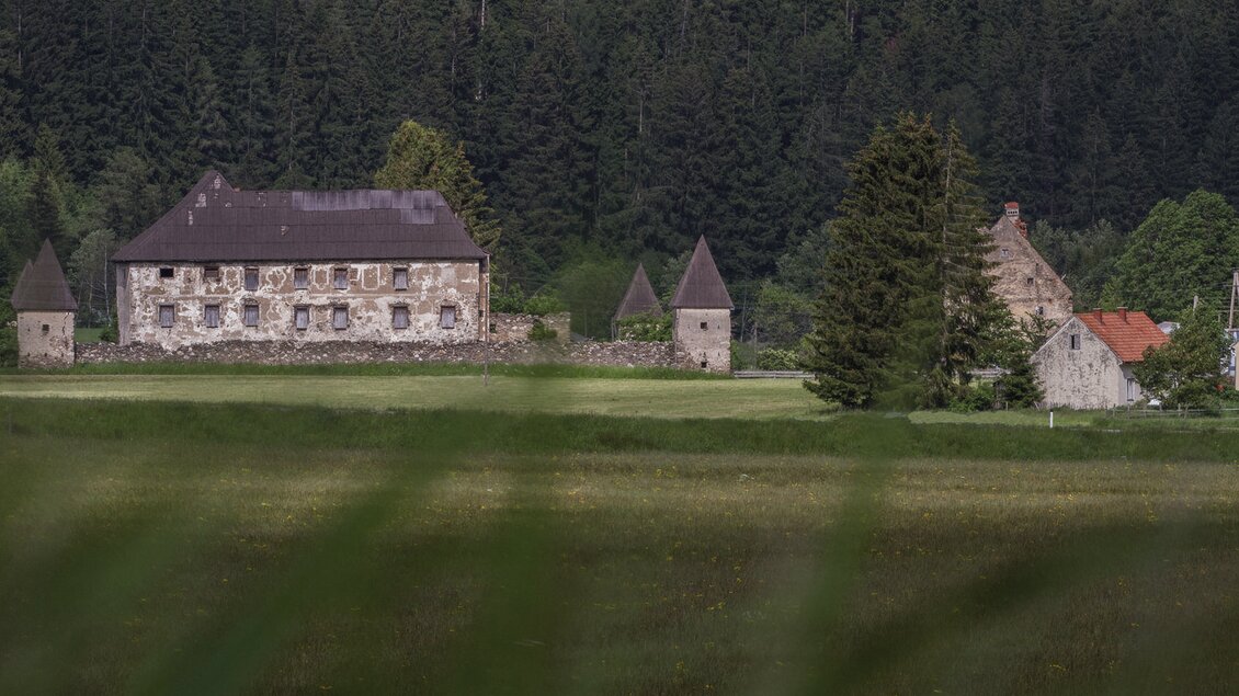 Ein altes, historisches Gebäude mit Türmen, umgeben von viel Grün und Wäldern. Im Hintergrund sind einige weitere kleine Häuser sichtbar. | © Erlebnisregion Murtal
